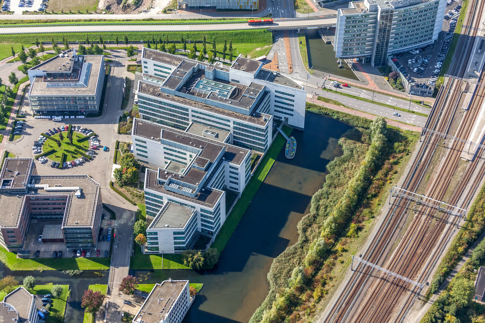 Luchtfoto van het D-Hub kantoorgebouwcomplex naast een spoorlijn en omgeven door water en wegen.
